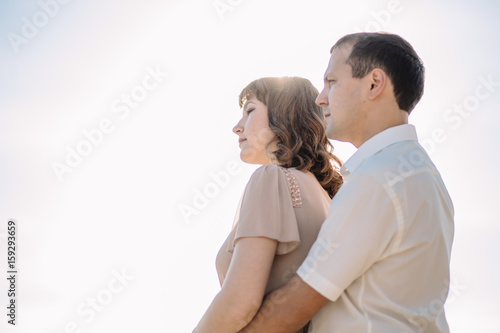 beautiful couple, the girl in the beige dress, the man in white shirt standing close to each other on the background of sky, sun, close-up, summer, heat, nature, love story