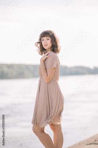 very beautiful, sexy, gentle, cute girl in beige dress standing on the banks of the river, nature, summer, smile