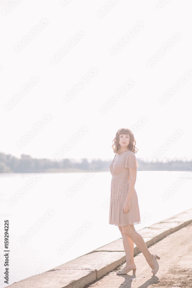 portrait of a woman, very beautiful, sexy, gentle, cute girl in beige dress stands on the banks of the river in the sun, outdoors in summer, smile