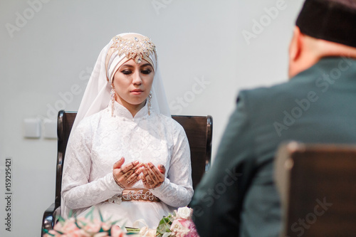 Islamic woman in wedding dress praying in mosque with mullah photo