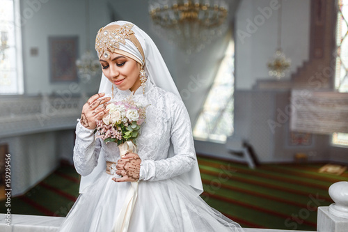 Muslim bride with jewelery in a headscarf hijab with a bouquet of flowers in a mosque photo