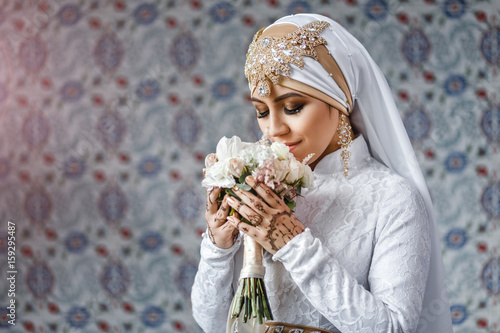 Muslim bride with jewelery in a headscarf hijab with a bouquet of flowers in a mosque photo