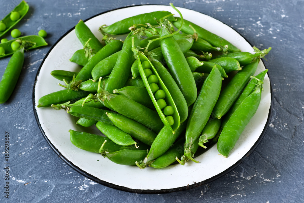 Fresh, young green peas in a plate on a concrete background. Bio food background. Fresh, young green peas in a plate on a concrete background. Bio food background.