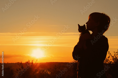 Children, pets, people and childhood concept. Cropped shot of a silhouette of a girl holding her kitten at sunset. Cropped shot of a cute little girl and kitten at sunset.