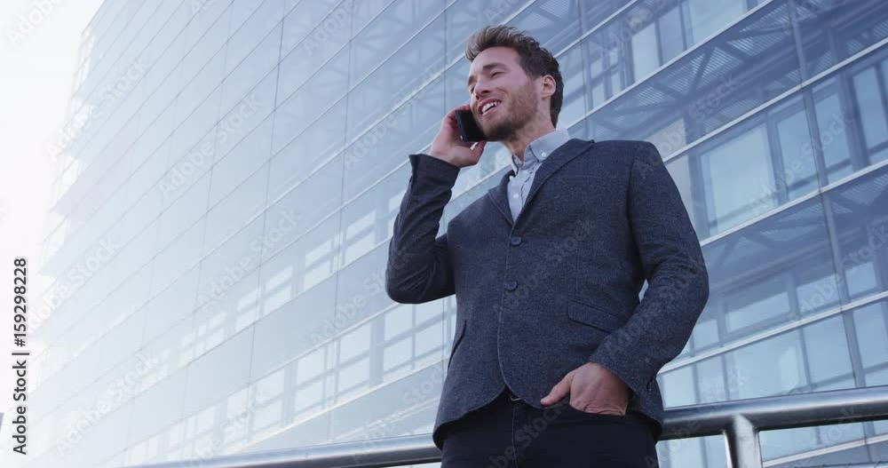 Smart phone man calling on mobile phone in city business district. Confident young business man talking on smartphone smiling happy wearing suit jacket outdoors. Urban male professional in 20s. Smart phone man calling on mobile phone in city business district. Confident young business man talking on smartphone smiling happy wearing suit jacket outdoors. Urban male professional in 20s.