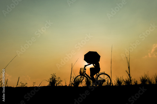 Silhouette of boy riding bicycle on sunset background.