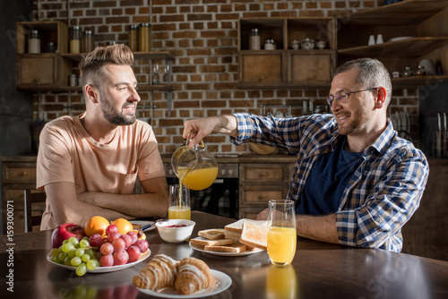 Happy homosexual couple having breakfast and talking at home