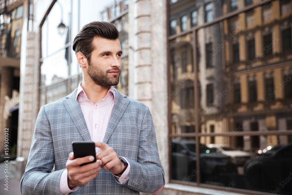 Handsome man in a jacket standing and holding mobile phone Handsome man in a jacket standing and holding mobile phone
