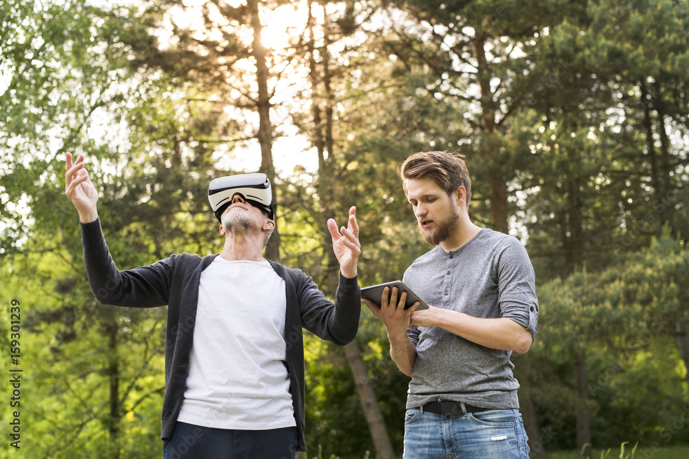 Young man and his senior father with VR glasses outdoors. Young man and his senior father with VR glasses outdoors.