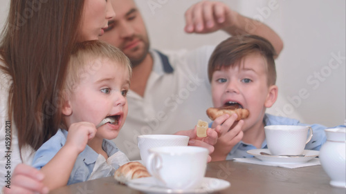 Two little boy kids having tea with pastry together with their parents