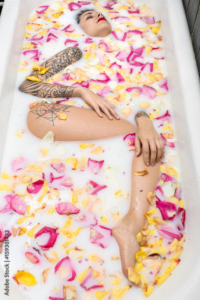 Charming girl with fancy tattoos lies in the white bath full of Charming girl with fancy tattoos lies in the white bath full of