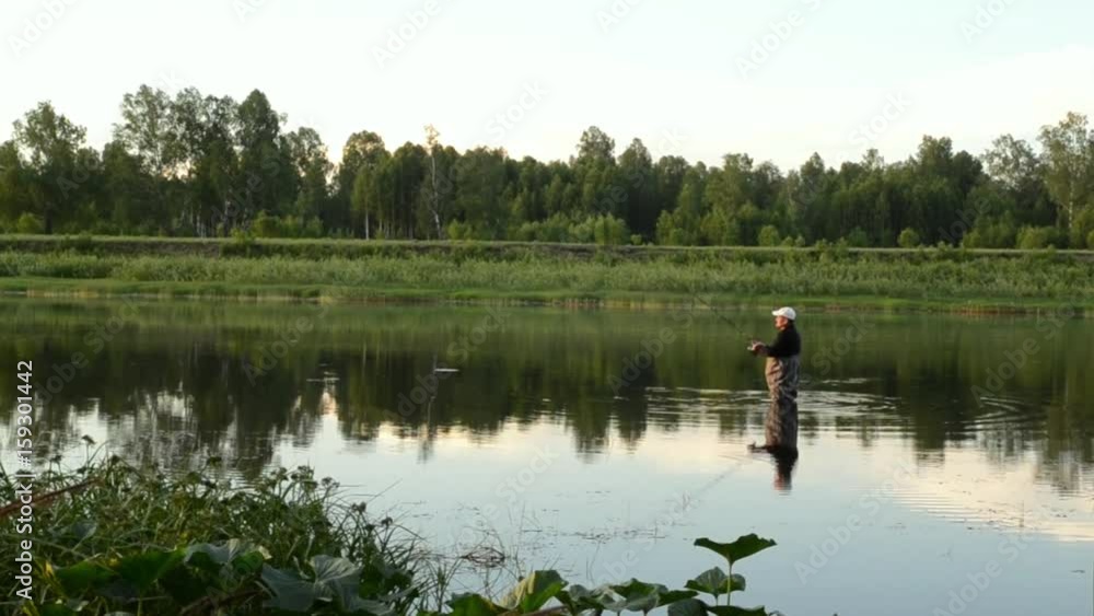 fisherman fishing in a calm river in the morning. Man in fishing gear stending in a river and throws a fishing pole fisherman fishing in a calm river in the morning. Man in fishing gear stending in a river and throws a fishing pole