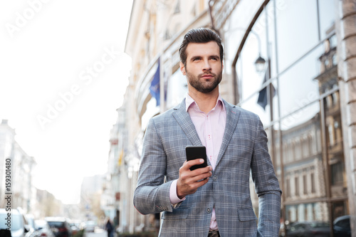 Handsome man in a jacket walking and holding mobile phone