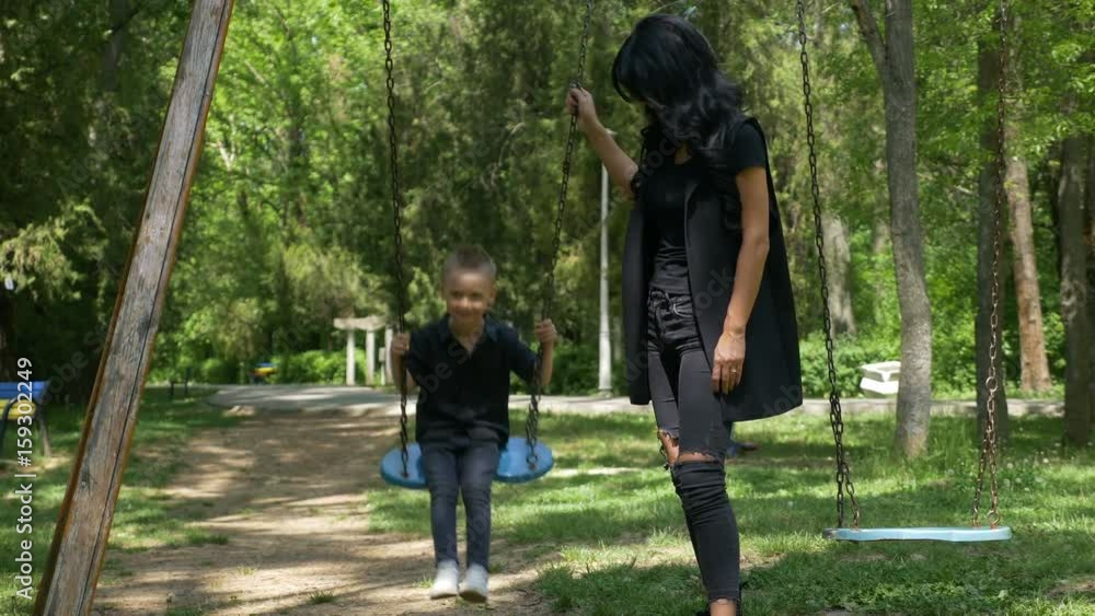Young single mother pushing child on a swing set Young single mother pushing child on a swing set