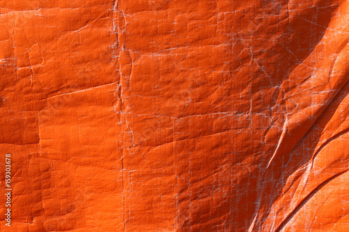 Orange color plastic tarpaulin covering, polyester fabric texture.