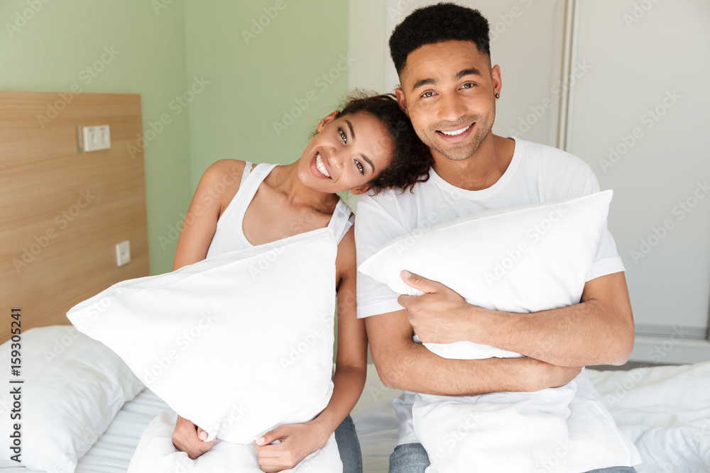 Cheerful young african loving couple sitting on bed Cheerful young african loving couple sitting on bed