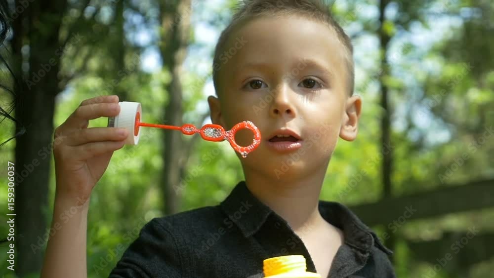 Closeup of happy cute boy blowing colored soap bubbles in sunny park Closeup of happy cute boy blowing colored soap bubbles in sunny park