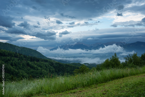 Mountain landscape shortly after spring rain. Slovenian Alps. Forest Road, venerable tree, fog, clouds and peaks. The village of Jamnik Slovenia.