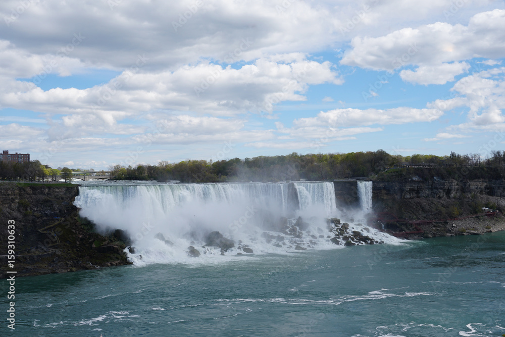 Niagara Falls waterfall on bright spring day with clouds and blue sky as seen from Ontario, Canada