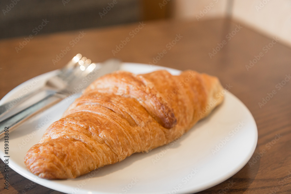 Warm fresh Croissants on a white plate with fork and knife in the coffee shop.(Selective focus with shallow depth of field) Warm fresh Croissants on a white plate with fork and knife in the coffee shop.(Selective focus with shallow depth of field)