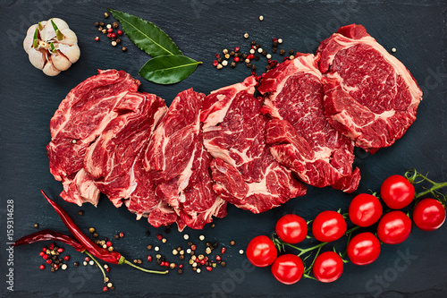 Fotografia Fresh raw beef steaks with pepper and tomatoes on black slate board