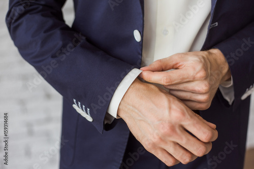 Closeup of elegant young fashion man dressing up for wedding celebration. Color close up image of male hands. Handsome groom dressed in modern blue formal suit, white shirt getting ready for event. © Andrii Oleksiienko
