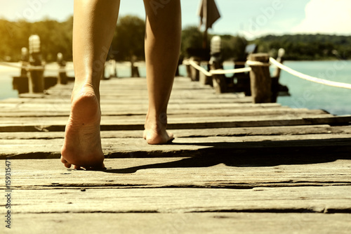 Bare feet woman walking on the walkway wood in sea with sunlight