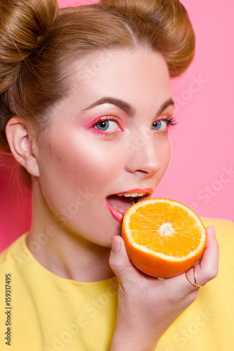 portrait of cute attractive blonde young woman with colorful makeup with oranges in her fingers