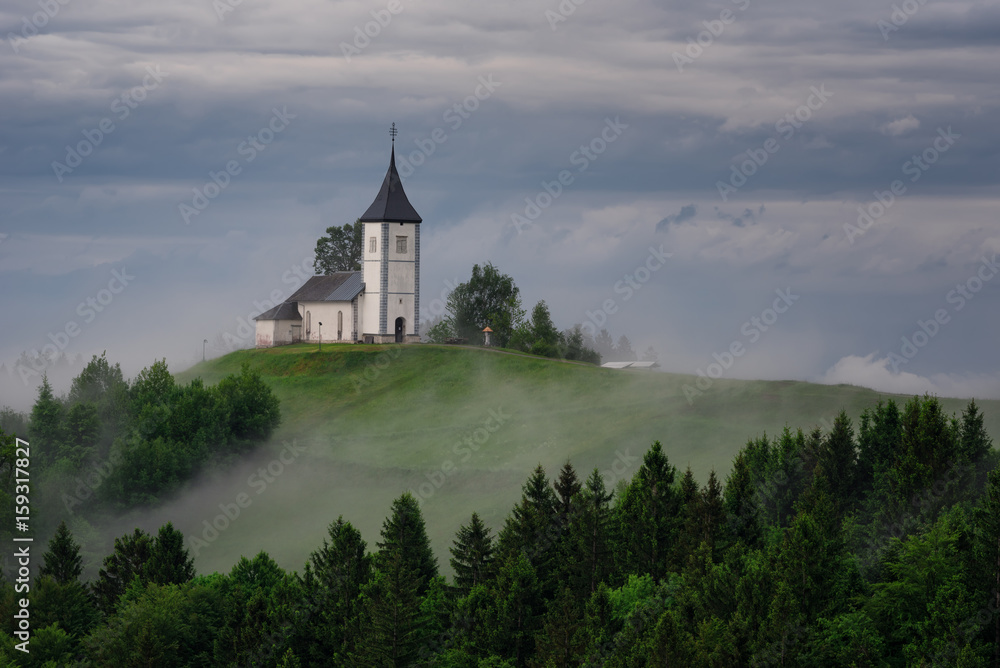 Jamnik church on a hillside in the spring, foggy weather at sunset in Slovenia, Europe. Mountain landscape shortly after spring rain. Slovenian Alps. Jamnik church on a hillside in the spring, foggy weather at sunset in Slovenia, Europe. Mountain landscape shortly after spring rain. Slovenian Alps.