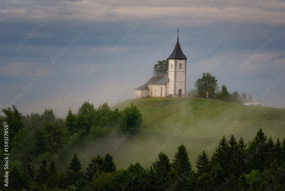 Jamnik church on a hillside in the spring, foggy weather at sunset in Slovenia, Europe. Mountain landscape shortly after spring rain. Slovenian Alps. Jamnik church on a hillside in the spring, foggy weather at sunset in Slovenia, Europe. Mountain landscape shortly after spring rain. Slovenian Alps.
