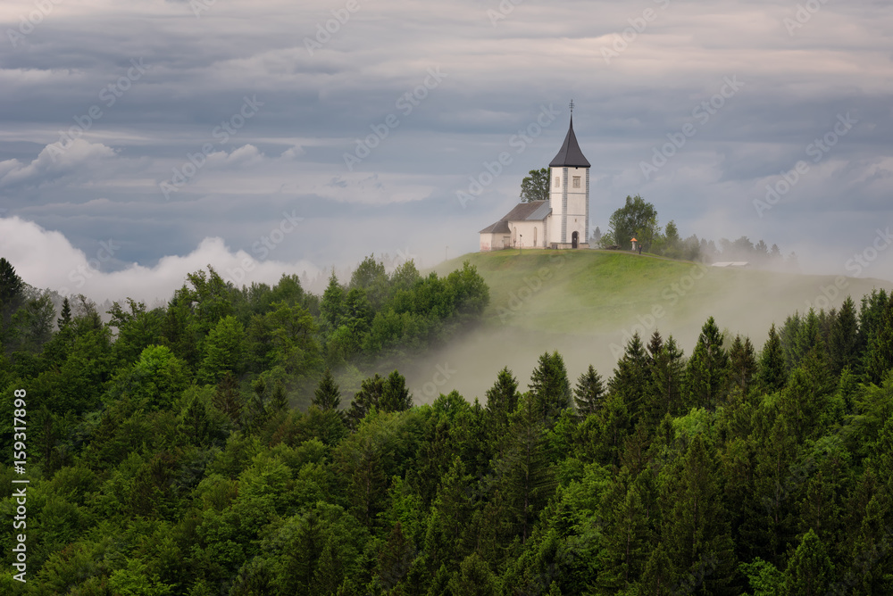 Jamnik church on a hillside in the spring, foggy weather at sunset in Slovenia, Europe. Mountain landscape shortly after spring rain. Slovenian Alps. Jamnik church on a hillside in the spring, foggy weather at sunset in Slovenia, Europe. Mountain landscape shortly after spring rain. Slovenian Alps.