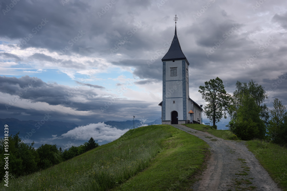 Jamnik church on a hillside in the spring, foggy weather at sunset in Slovenia, Europe. Mountain landscape shortly after spring rain. Slovenian Alps. 