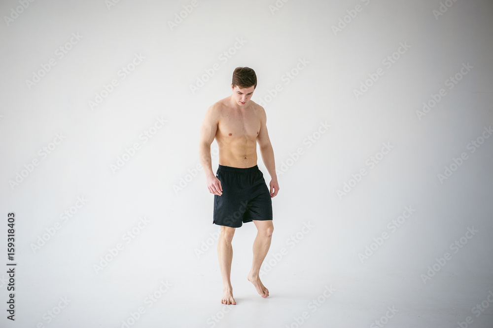 portrait young sexy handsome man of strong Athlete's body with bare torso, Dressed in a black sports shorts, Posing on white studio background