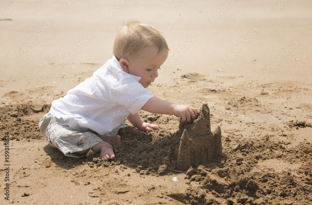 One year old baby boy playing on the beach with a sand castle One year old baby boy playing on the beach with a sand castle