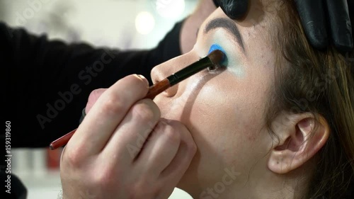 Man makeup artist making the face art with blue shadows closeup
