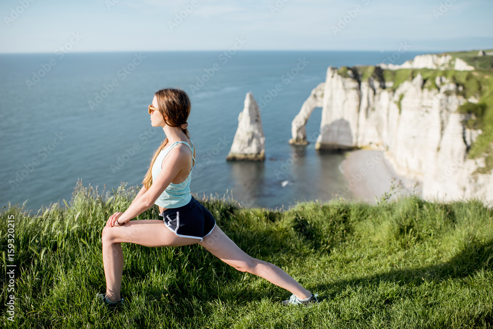 Young woman in sportswear streching outdoors on the beautiful rocky coastline background near Etretat town in France