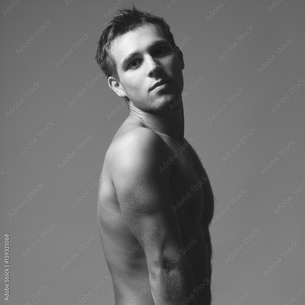 Fototapeta premium Bodybuilding and body sculpture concept. Beautiful (handsome) muscular male model with perfect body posing over blue background. Black and white studio shot