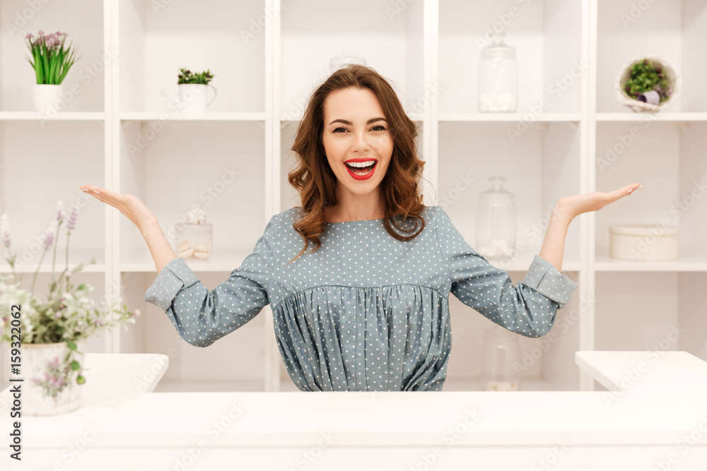 Smiling young lady sitting in shop over shelf background Smiling young lady sitting in shop over shelf background