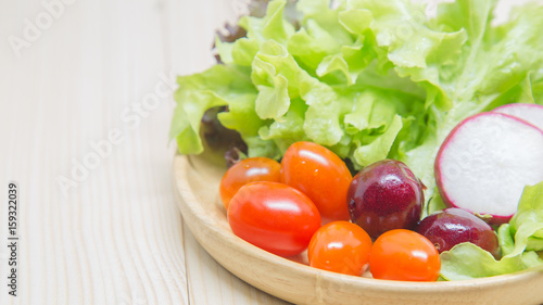 Salad in a wooden bowl on a wooden table, lettuce, tomatoes, cherries.