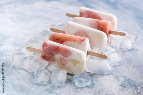 Healthy vegan coconut ice cream popsicles with peach White and red popsicles on melted ice