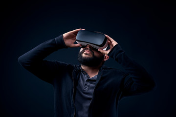 Young hipster bearded man wearing virtual reality goggles. Black background studio VR concept.