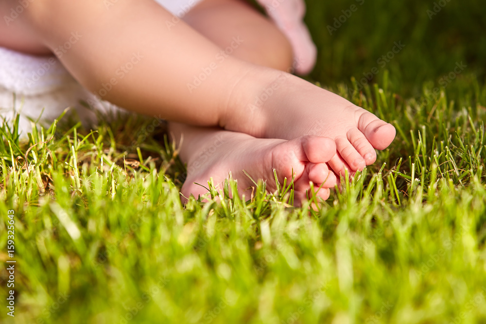 Close-up of the little baby legs on a green grass in the city park. Close-up of the little baby legs on a green grass in the city park.