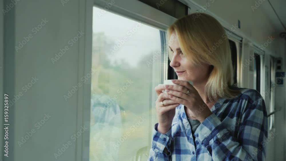 A woman with a cup of coffee looks out the window from a train. Love to travel A woman with a cup of coffee looks out the window from a train. Love to travel