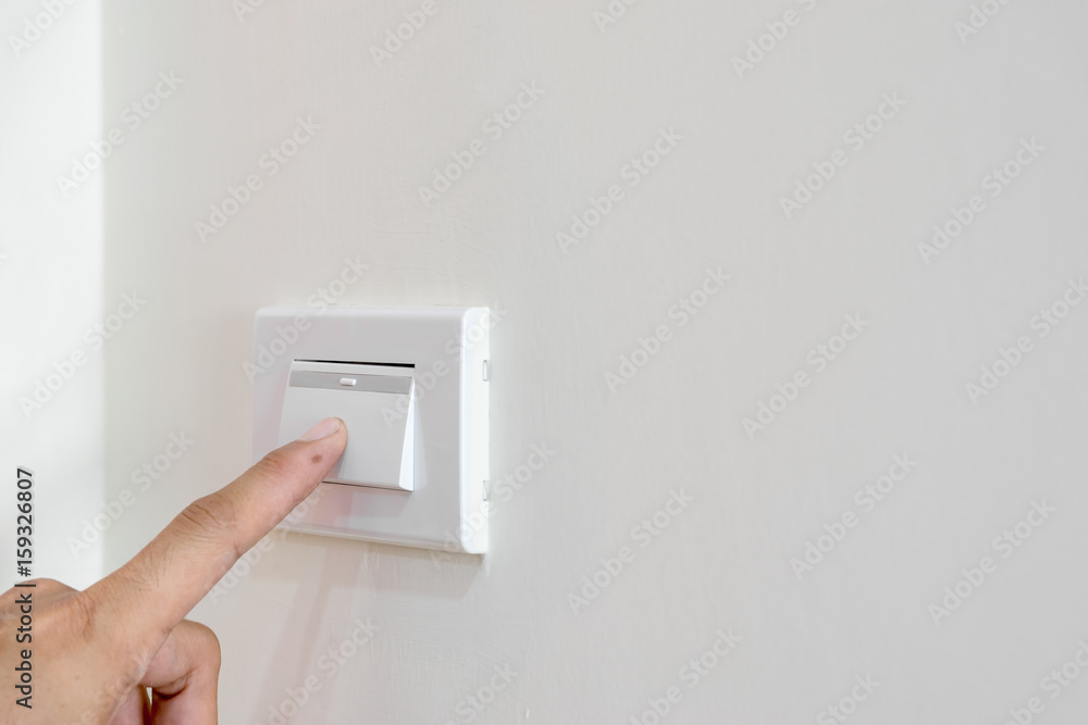 Men's fingers are extended to open the light switch on the wall. Men's fingers are extended to open the light switch on the wall.