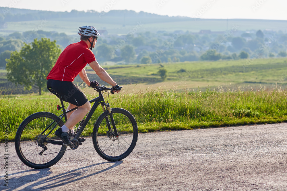 Attractive man in white helmet riding a bike on country road. Attractive man in white helmet riding a bike on country road.