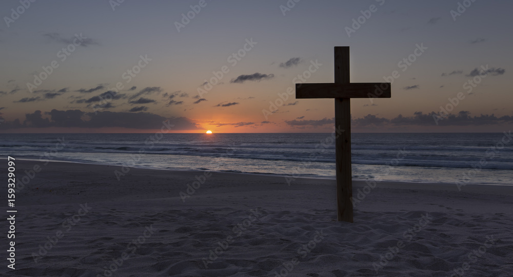 An old cross on sand dune next to the ocean with a calm sunrise An old cross on sand dune next to the ocean with a calm sunrise