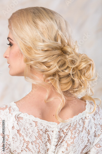 fashionable gown  beautiful blonde model  bride hairstyle and makeup concept - back view on young charming lady in wedding white dress standing indoors on light background  pretty woman posing