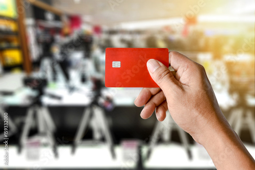 a hand holding credit card on blurred camera shop store