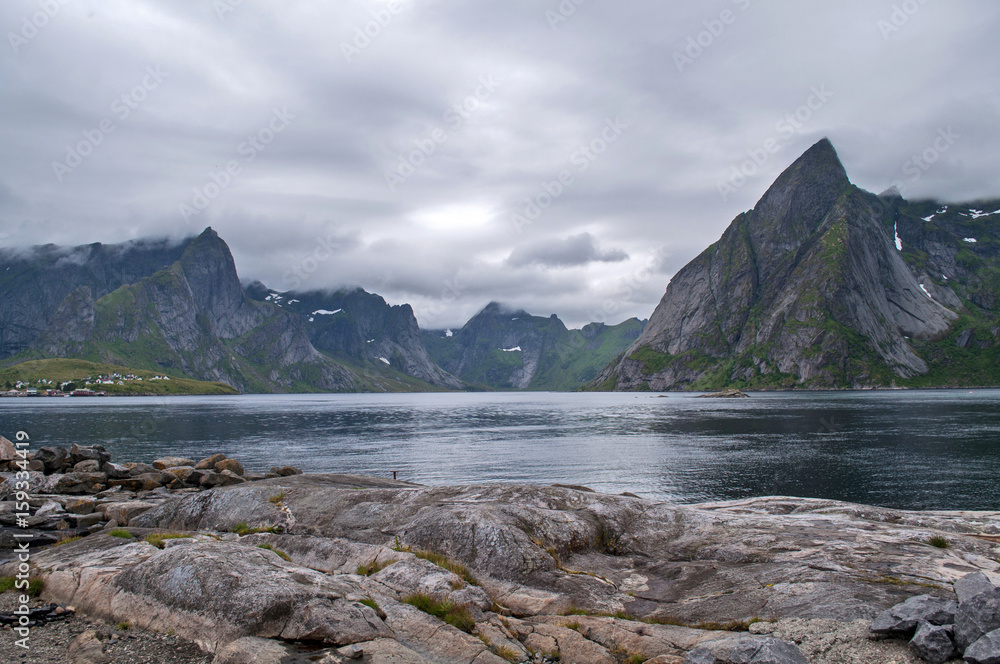 Spiky rocky mountains in the clouds towering over the lake (Lofoten, Norway)