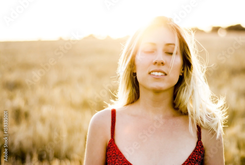 Beautiful blond woman in a red dress, on a wheat field at sunset